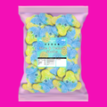 A bag of vegan blue and yellow skull-shaped gummy candies, shown against a solid bright pink background. The packaging is a light pink resealable pouch with a clear window displaying the gummies, and a central label reads 'Skittles Vegan Blue & Yellow Skulls'.